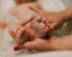 Close-up of a baby's feet during a bath, with an adult's hands gently holding them.