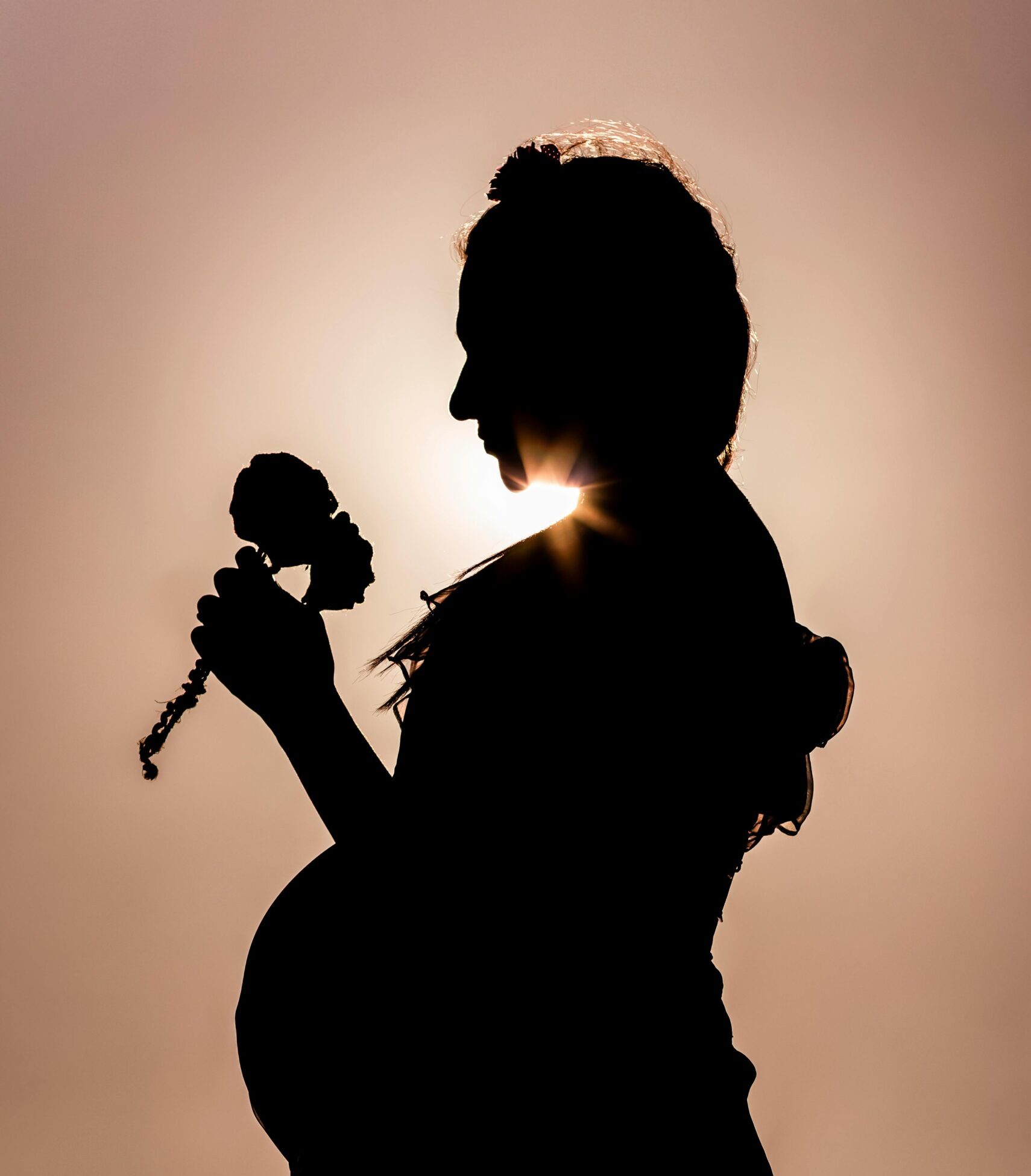 Pregnant woman holding a flower in silhouette against the sunset.